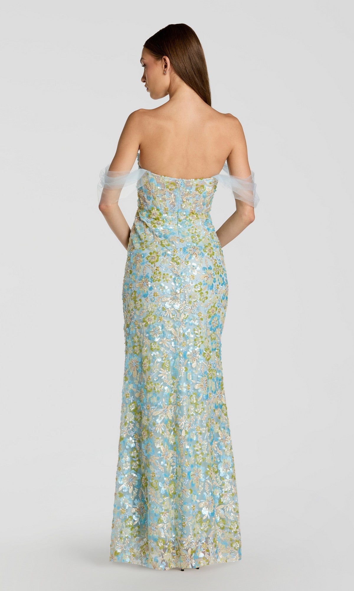 A woman is shown from the back against a plain light background, wearing the Long Formal Dress: Mac Duggal 69045—a strapless, floor-length gown featuring blue floral embroidery and sheer off-the-shoulder sleeves.
